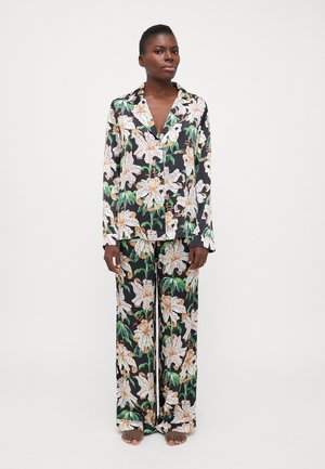 Blomstret pajamasæt med en sort baggrund, der har store hvide liljer og grønne blade. Løse, langærmede toppe og brede bukser.