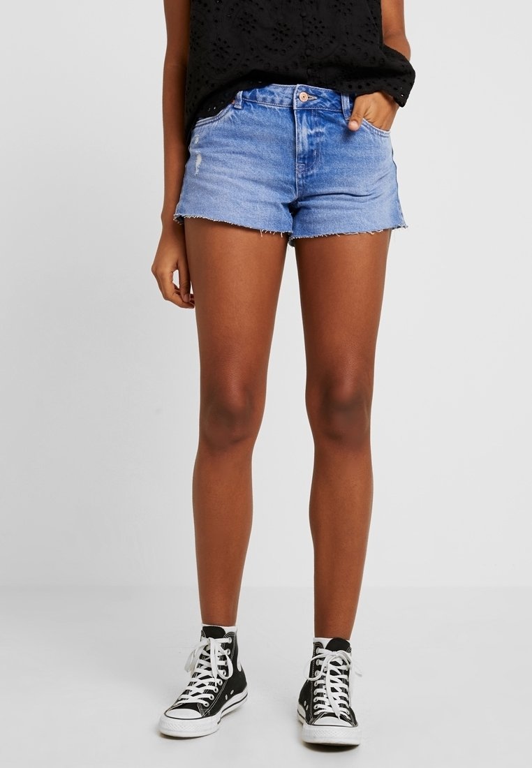 Vaaleansiniset farkkushortsit, joissa on revitty helma. Varustettu vetoketjusekalla ja etutaskuilla. Yhdistetty mustiin korkeisiin tennareihin.