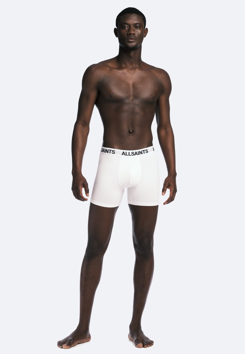 Caleçons boxers blancs avec un logo "ALLSAINTS" noir sur la ceinture. Le matériau semble lisse et ajusté, avec un design sans couture.
