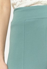 Sukně s vysokým pasem v odstínu teal, vyrobená z hladké tkaniny, s krytou kapsou a pevným designem s čistými liniemi.