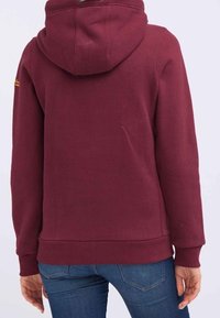 Bordowy hoodie z gładką teksturą, posiadający kieszeń kangurzą, ściągacze przy rękawach oraz u dołu, widoczny szczegół logo z tyłu.