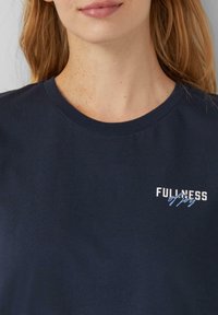 T-shirt en coton navy à manches courtes et col rond. Présente le texte blanc "PLÉNITUDE de joie" brodé sur la poitrine gauche.