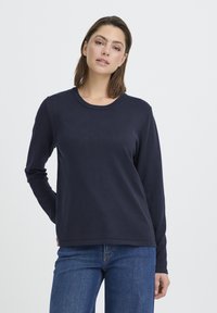 T-shirt à manches longues bleu marine en coton doux, doté d'un col rond classique et d'une coupe décontractée, associé à un jean bleu.