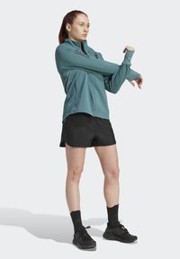Teal lightweight jacket with zip front, features black accents. Worn over black shorts and paired with black athletic shoes and socks.