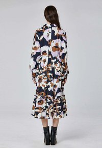 Robe à manches longues avec un motif abstrait audacieux dans des teintes marron, blanc et violet, dotée d'un ourlet à volants superposés. Texture mate, design à col.