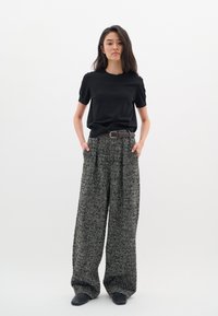 T-shirt nero a maniche corte abbinato a pantaloni a gamba larga con motivo houndstooth. I pantaloni presentano delle pieghe, indossati con una cintura marrone e scarpe nere.