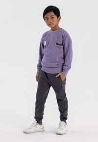 Paarse sweatshirt met grafische prints, gecombineerd met donkergrijze joggingsbroek. Witte sneakers maken de outfit af. Eenvoudig, casual ontwerp.
