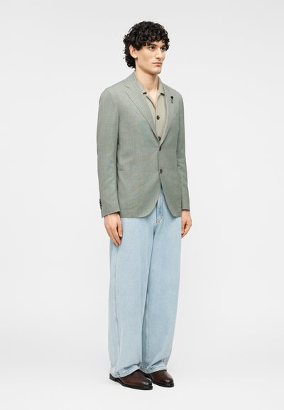 Ανοιχτό πράσινο καρώ σακάκι με δύο εμπρόσθιες τσέπες, συνδυασμένο με μπεζ πουκάμισο και φαρδιά ανοιχτό μπλε τζιν, ολοκληρωμένο με καφέ παπούτσια.