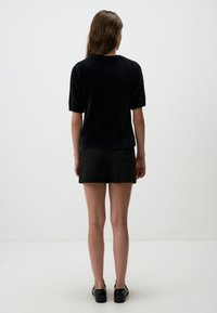 Czarna bluzka z krótkim rękawem wykonana z miękkiego materiału, charakteryzująca się luźnym krojem i prążkowanym dekoltem. Noszona z czarnymi szortami i płaskimi butami.