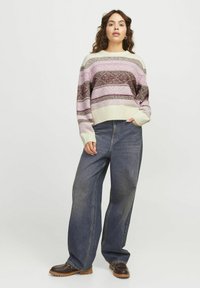 Gebreide pullover met horizontale strepen in tinten roze, bruin en crème; brede blauwe denim jeans; bruine veterschoenen.