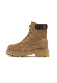Bota de tobillo de ante marrón con un acento de cuero marrón oscuro en el puño, que presenta ojales de metal y una suela de goma rugosa y con diseño.