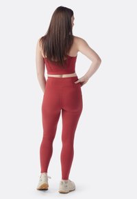 Rotes sportliches Crop-Top und Leggings, die ein enges Design und eine glatte Textur bieten. Die Leggings haben einen hohen Taillenbund und Gesäßtaschen.