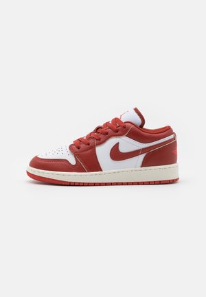 Zapatilla baja con paneles de cuero rojos y blancos, cordones rojos y un logo rojo de Nike en el lateral, mostrada sobre un fondo blanco.