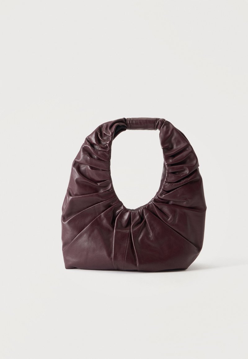 Sac à main en cuir souple bordeaux foncé avec des détails froncés et une poignée arrondie, posé debout sur un fond clair uni.