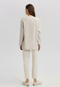 Lys beige langærmet top med en afslappet pasform, lige kant og minimale syninger, parret med cremede, tætsiddende bukser og beige sneakers.