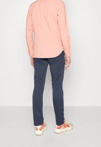 Hellrosa Hemd mit langen Ärmeln, marineblaue Hose und mehrfarbige Sportschuhe. Einfaches Design mit Knöpfen an den Ärmeln.