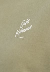 Tejido verde oliva con una textura suave que presenta texto bordado en blanco: "Café Kitsuné" sobre "PARÍS" centrado en el diseño.