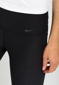 Leggings neri Nike con tessuto morbido e elastico, vita alta, caratterizzati da un piccolo logo scuro nella parte anteriore.