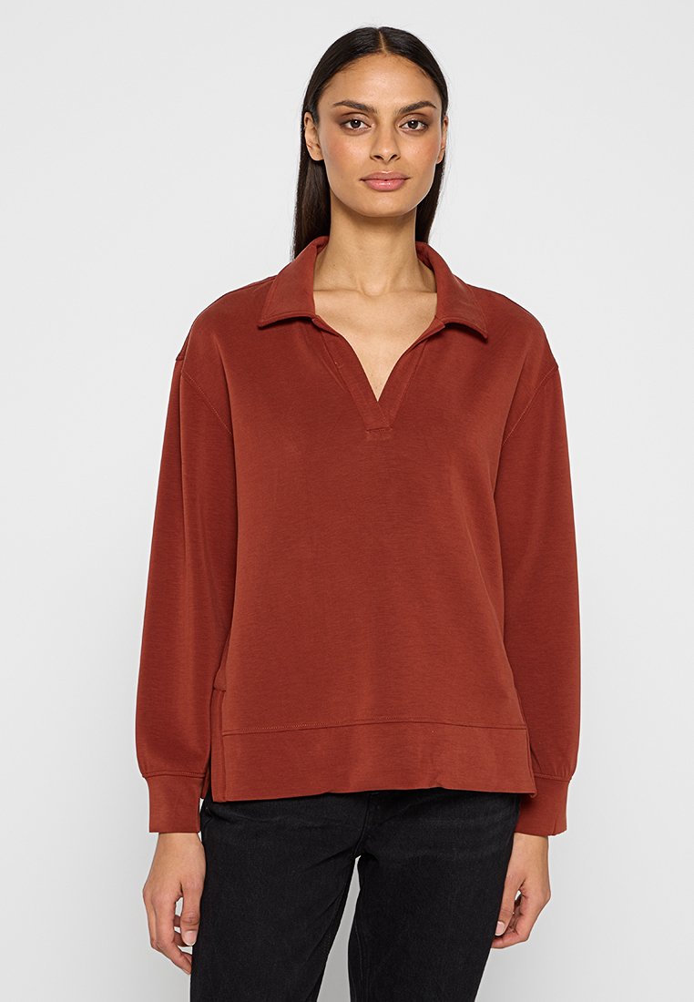 Pull en couleur rouille avec un col, des manches longues, une coupe ample et un ourlet côtelé. Le matériau a l'air doux avec une texture lisse.