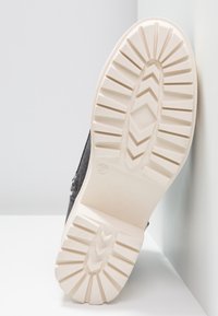 Suola della scarpa con una parte superiore in grigio scuro texture, suola in gomma chiara con motivo a zigzag e ampi intagli per la trazione.