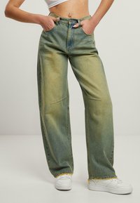 Lys grønne brede denimjeans med frynset kant, fem lommer og knappestolpe. Kombinert med hvite sneakers.