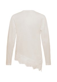Haut crème à manches longues vu de dos, avec un ourlet en dentelle asymétrique sur le bas.