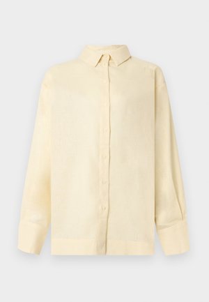 Chemise crème à manches longues avec boutons, col structuré et larges poignets, présentée sur un fond uni clair.