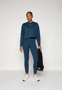 Temno modra športna obleka, ki vključuje kratko jopico in pajkice, izdelana iz gladkega blaga, z majhnim Nike logotipom na prsih in ob strani.