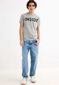 Camiseta gris de manga corta con la palabra "INSIDE" impresa en negro, combinada con jeans rectos de color azul claro y zapatillas blancas con detalles en marrón.