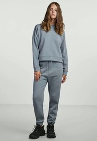 Gai pelēks kokvilnas krekls ar apaļu izgriezumu un brīvu piegriezumu, savienots ar atbilstošām pelēkām sporta biksēm ar elastīgu jostu un ribu aprocēm.