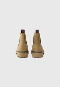 Botas de tobillo de ante marrón con paneles laterales elásticos y una suela de goma texturizada, que cuentan con lengüetas para ponerse fácilmente.