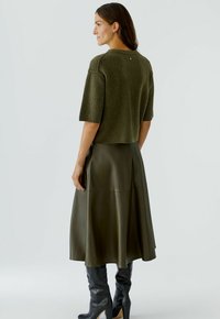 Olivgr�üner, kurz geschnittene Pullover mit kurzen Ärmeln, kombiniert mit einem fließenden, dunkelgrünen Lederrock und kniehohen, schwarzen Stiefeln, minimalistisches Design.