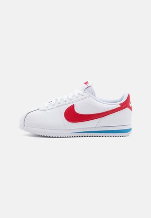 White sneaker featuring a red swoosh, blue accent on the sole, and white laces. Textured upper with stitched detailing. Classic design.