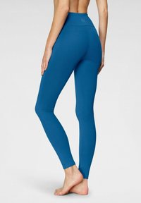 Leggings a vita alta di colore teal uniforme, realizzati in tessuto elasticizzato, con una texture liscia e un design aderente che si adatta alle gambe.