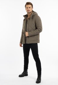 Quiltet olivengrøn jakke med hætte, trykknaplukning, sidelommer og diamantmønster, parret med sorte slim-fit bukser og sorte snørebåndsstøvler.