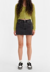 Svart denimkjol med fransad nederkant, parat med en kort grön fluffig cardigan. Skorna är svarta och vita sneakers med vita strumpor.