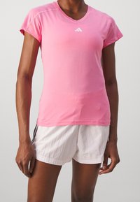 Pink short-sleeve athletic shirt with a V-neck and white Adidas logo. Lightweight fabric, fitted design, paired with white athletic shorts.