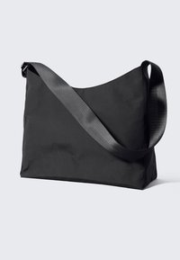 Crna ramena torba od najlona sa širokim remenom, koja ima mekan, strukturiran dizajn i ravno dno za stabilnost. Nema vidljivih metalnih dijelova ili ukrasa.