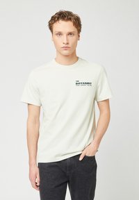 Lichtgroene katoenen T-shirt met korte mouwen, ronde halslijn en "THE BOTANIST" in donkergroen gedrukt op de linkerborst.
