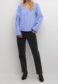 Haut à manches longues bleu clair, bien côtelé, avec un col rond et des poignets évasés, associé à un jean noir et des bottines.