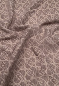 Textureret stof i lys taupe med et gentagende cirkulært mønster. Materialet ser ud til at være vævet og blødt, hvilket skaber bløde folder.