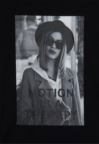 Donna con un cappello, occhiali da sole e cappotto sopra un felpa si trova all'aperto; il testo dice "IL MOVIMENTO È UNA TERAPIA."