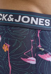 Mornarske bokserice s cvjetnim i flamingo uzorkom, s teksturiranim elastičnim pojasom na kojem je tekst "CK&JONES" u bijeloj i tirkiznoj boji.
