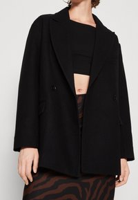 Sort uldblanding frakke med slået krave, dobbelte knapper og sidelommer. Let oversized pasform med en glat tekstur.
