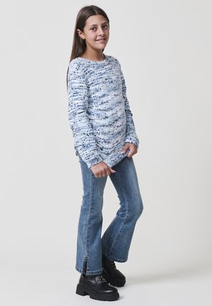 Blau-weißer gestrickter Pullover mit Struktur, langen Ärmeln und rundem Halsausschnitt, kombiniert mit hellblauen Schlagjeans und schwarzen Schnürstiefeln.