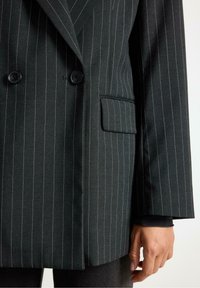 Sort blazer med striber, der har dobbeltknaplukning, udskårne revers og en sidelomme. Glat stof med en subtil glans.