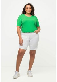 Camisa verde de manga corta combinada con pantalones cortos blancos. La parte superior tiene un escote redondo; los pantalones cortos tienen un corte relajado y son de largo hasta la rodilla.