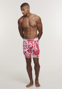 Bóxers ajustados de color rojo y blanco con un diseño gráfico que presenta formas abstractas y texto, fabricados con tela elástica y una cinturilla con marca.