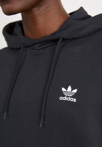 Sudadera negra hecha de una tela suave con un logo blanco de Adidas y tres rayas en el lado izquierdo del pecho, y con cordones para ajuste.
