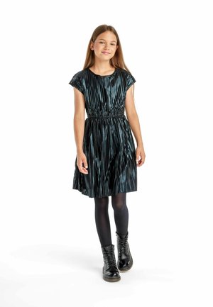 Robe plissée bleu foncé avec des manches courtes et une taille élastique, associée à des collants noirs et des bottes à lacets. Le tissu a une finition brillante.